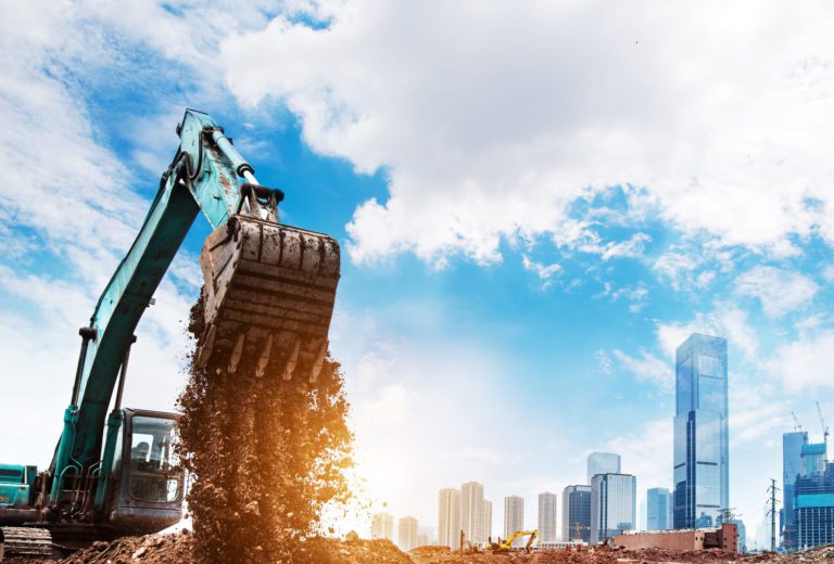 O que é LCI: uma máquina de construção civil e em segundo plano alguns prédios.