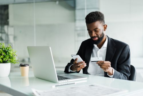 Títulos Bancários: um homem negro com o celular na mão e um cartão de crédito em outro.