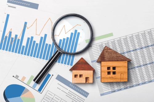 fundos imobiliarios: imagem de duas casinhas de madeiras em cima da mesa com uma lupa, mais alguns gráficos e tabelas.