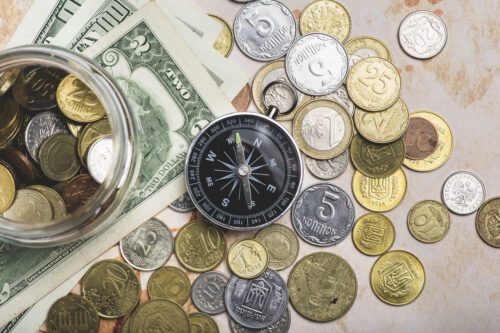 marco cambial: várias moedas de diferentes países sob a mesa e uma búsula e algumas notas de dinheiro.