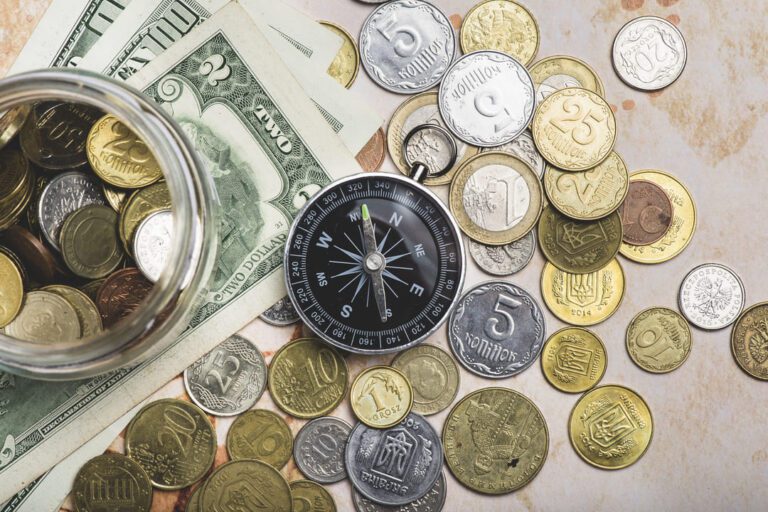 marco cambial: várias moedas de diferentes países sob a mesa e uma búsula e algumas notas de dinheiro.