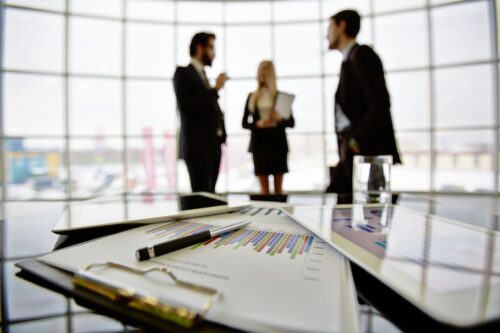 cvm: na mesa, uma planilha mostrando as oscilações do mercado financeiro e três pessoas conversando sobre as questões financeiras do país.