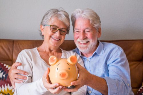 investimento para aposentadoria: dois senhores sorrindo, uma mulher e um homem, segurando um cofrinho de porquinho nas mãos.
