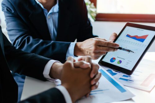 assessoria de investimentos: um homem explicando as oscilações do mercado financeiro na tela de um tablet para outra pessoa.