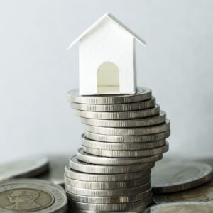 Casa de papel sobre uma pilha de moedas na cor prata para ilustrar a metáfora do IFIX, índice que avalia o desempenho de fundos imobiliários