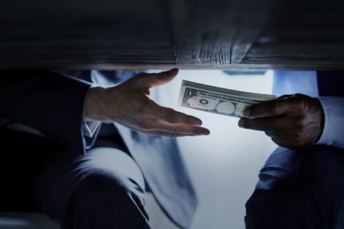 insider trading: duas pessoas passando dinheiro por debaixo da mesa.