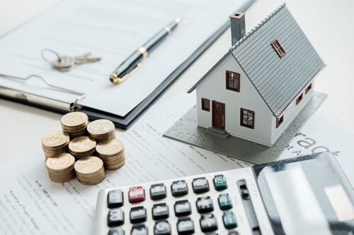 Composição com moedas, contrato, caneta, calculadora e maquete de uma casa sobre uma superfície branca para ilustrar ps trâmites do inventário de bens