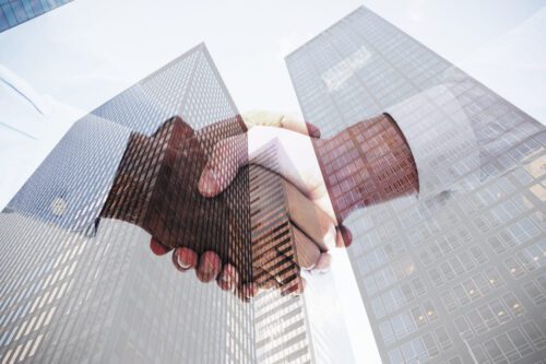 empresa de capital fechado: em primeiro plano um aperto de mão e em segundo dois prédios.