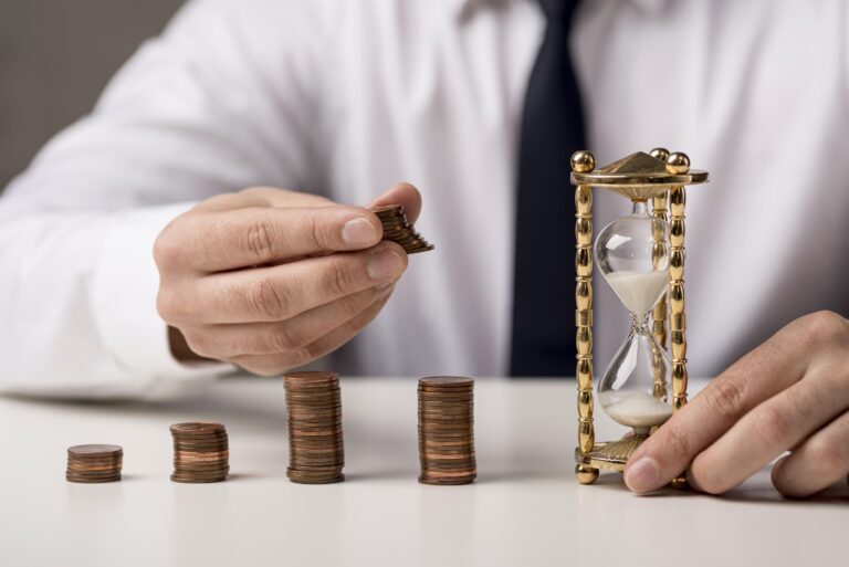 duration: pilhas de moedas na cor de bronze e uma ampulheta ao lado.