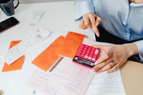 ICMS: uma pessoa usando uma calculadora roxa e algumas notas e papeis em cima da mesa.