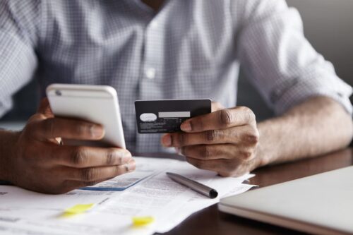 cartão de crédito: uma pessoa segurando um cartão de crédito e olhando para o celular.