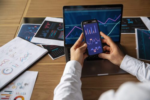 XP: uma pessoa analisando as oscilações do mercado financeiro no celular e no notebook.