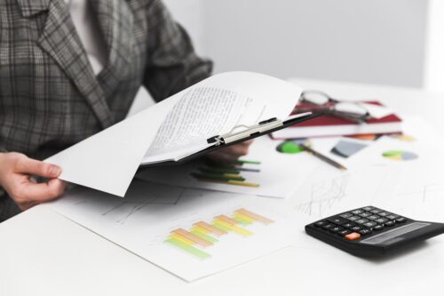 arcabouço fiscal: uma pessoa com papéis em cima da mesa, mais uma calculadora e lápis e bochada, lendo umas folhas em sua mão.