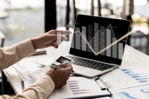 Indicadores financeiros: um computador e uma pessoa analisando gráficos de barras.