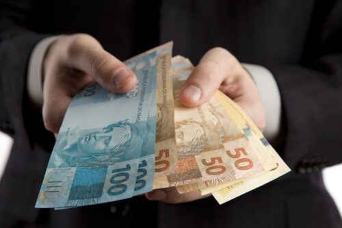 LFT: uma pessoa segurando notas de dinheiro brasileiro nas mãos, notas de 100 reais e 50 reais.