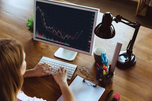 Price Action: uma pessoa analisando as oscilações do mercado financeiro por meio do computador, ao seu lado tem papel, caneta, tesoura, régua.
