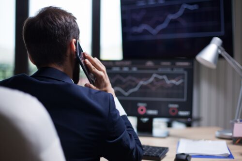 Homem com celular no ouvido olhando tela do computador que ilustra gráficos de performance apontados para cima.