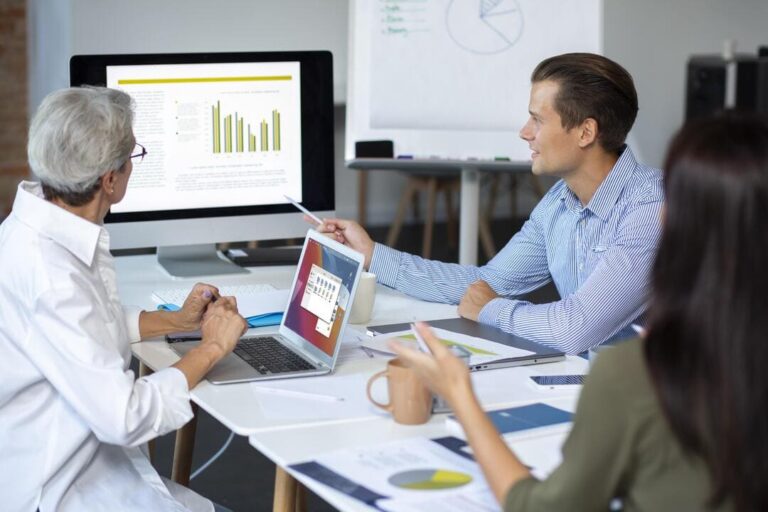 Pessoas reunidas em mesa de escritório olhando para o computador enquanto discutem os dados do ROE.
