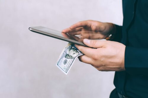 Mãos segurando celular e nota de dólar, representando o pagamento pelo FedNow.