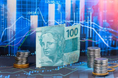 Nota de cem reais e moedas empilhadas, ao fundo destaca-se gráficos de investimentos, representando o Fi-Infra.