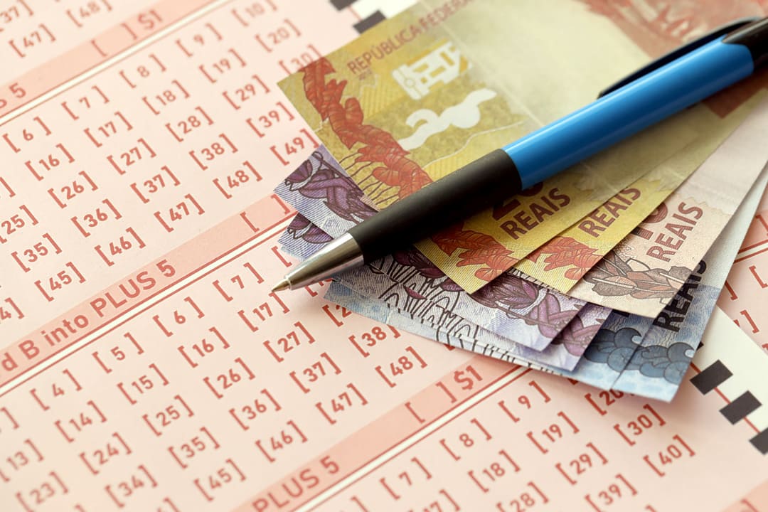 Volante da Mega da Virada com notas de real e caneta em cima.