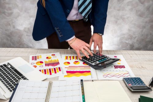 Homem de terno utilizando calculadora e examinando papéis de gráficos, representando a análise do patrimônio líquido.