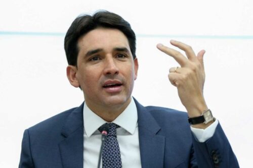 Ministro de terno e gravata com mão esquerda levantada