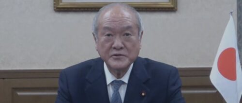 Ministro de finanças do Japão de terno com uma bandeira do Pais ao lado direito
