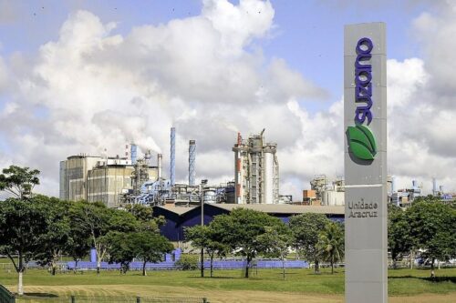 uma placa com o logo da suzano e uma fábrica ao fundo