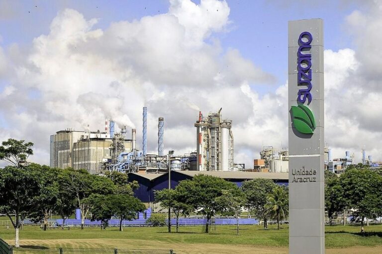 uma placa com o logo da suzano e uma fábrica ao fundo