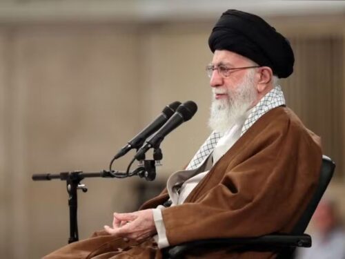 Presidente Ebrahim Raisi sentado de roupa marrom na frente de um microfone