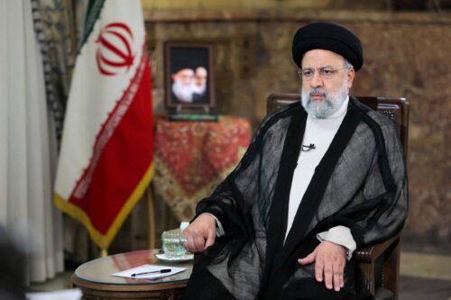 Ebrahim Raisi, falecido presidente do irã sentado em uma cadeira com bandeira atrás
