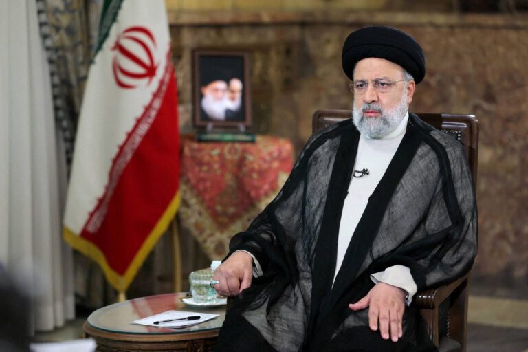 Ebrahim Raisi, falecido presidente do irã sentado em uma cadeira com bandeira atrás