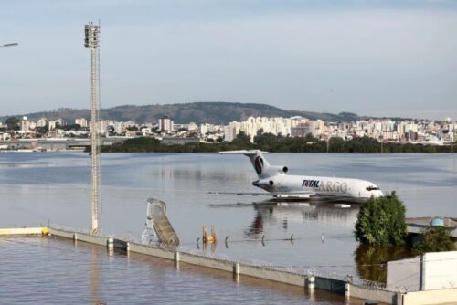 um avião de voo comercial na água com um corpo d'água e a cidade do RS ao fundo