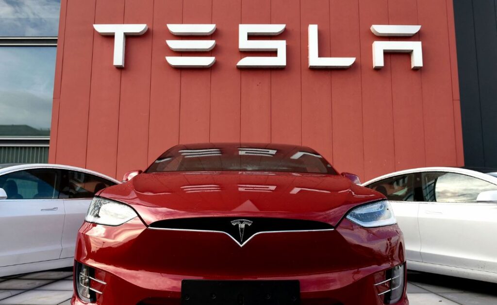 Carro da Tesla (TSLA; TSLA34) de Elon Musk, posicionado na frente do logo da empresa.