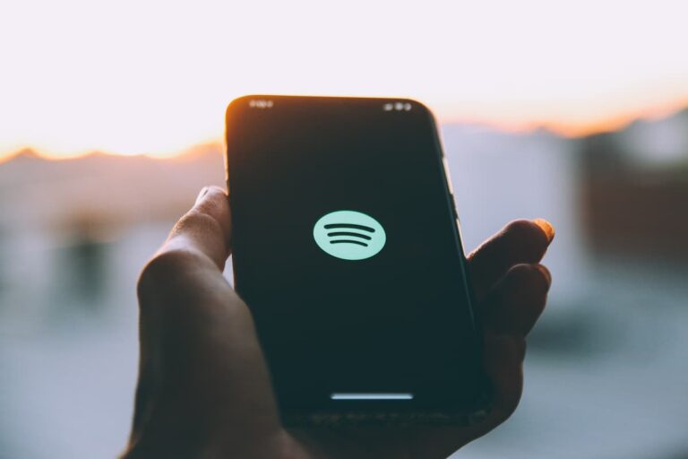 Mão segurando celular com logo do Spotify na tela, simbolizando Ações Spotify.