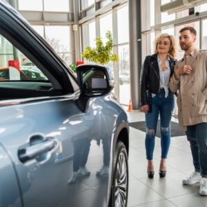 Pessoas em uma concessionária de carros, examinando um veículo novo, representando consórcios de veículos.