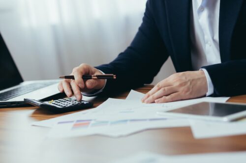 Profissional analisando documentos financeiros com calculadora e gráficos em uma mesa, representando securitizadoras e instituições financeiras.