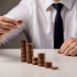 Homem em terno empilhando moedas, simbolizando o crescimento de investimentos, wealth management e planejamento financeiro.