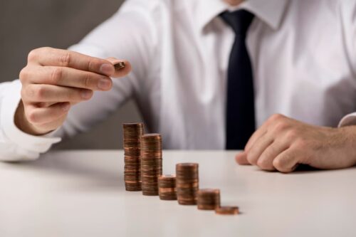 Homem em terno empilhando moedas, simbolizando o crescimento de investimentos, wealth management e planejamento financeiro.