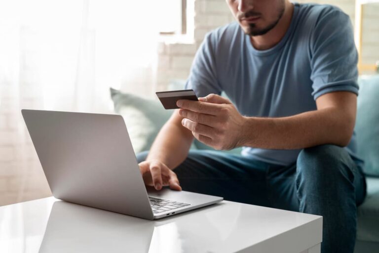 Homem usando laptop e segurando um cartão de crédito, representando a busca por entender o que é payback.