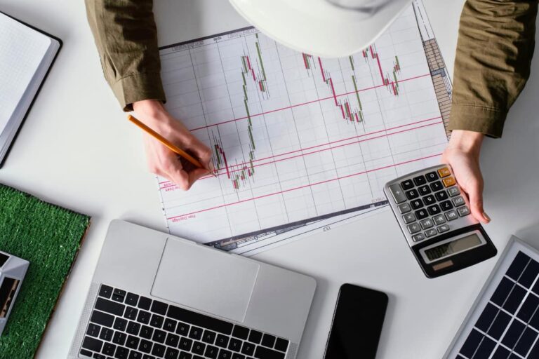 Pessoa analisando gráficos financeiros e calculando tendências, representando o estudo das ações mais baratas da Bolsa em 2024.