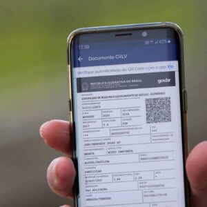 Pessoa exibindo o CRLV 2025 digital em um celular, com QR Code visível para autenticação do documento eletrônico.