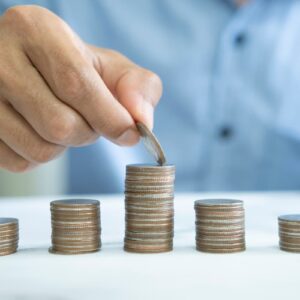 Pessoa empilhando moedas, representando a construção de um fundo de reserva para alcançar segurança financeira.