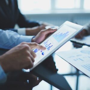Profissionais analisam gráficos em um tablet, discutindo estratégias de investimento, capex e opex em uma reunião corporativa.