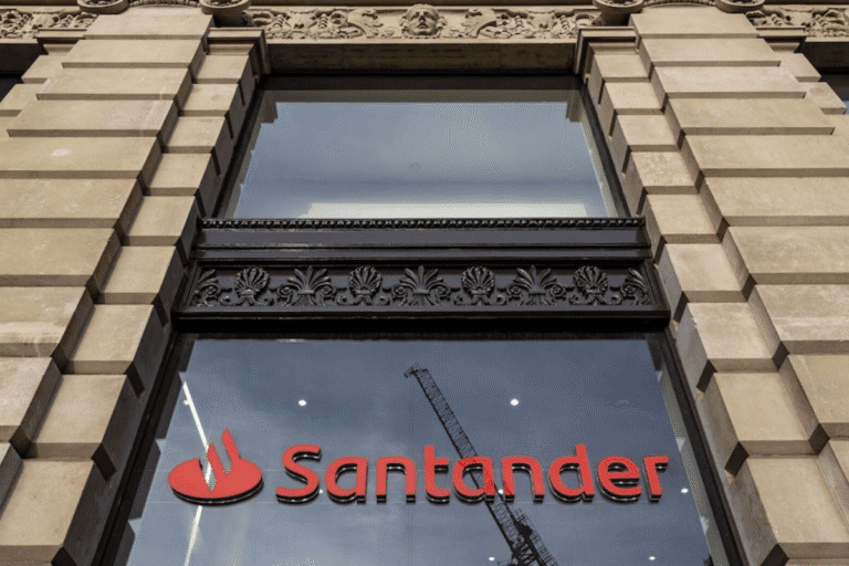 Imagem da fachada do banco Santander com foco na sua logomarca, refletindo a arquitetura de um edifício antigo, em meio a debates sobre contratação de executivo investigado por fraude.