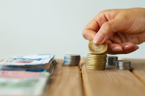 Pessoa empilhando moedas, representando o investimento em ações da B3 que custam menos de 10 reais.