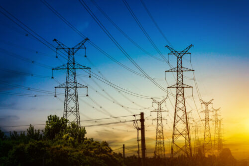 Pilares e torres de eletricidade contra um pôr do sol.