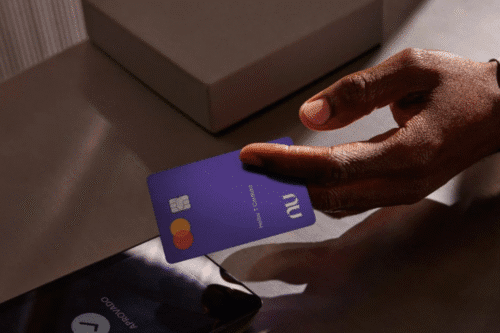 Foto de uma pessoa segurando um cartão da Nubank em frente a um telefone.