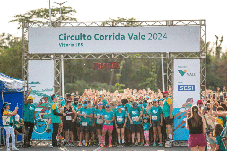 Participantes na Corrida Vale 2024 em Vitória, ES, reunidos na largada da corrida com inscrições de corrida visíveis e um grande banner acima com o nome do evento.